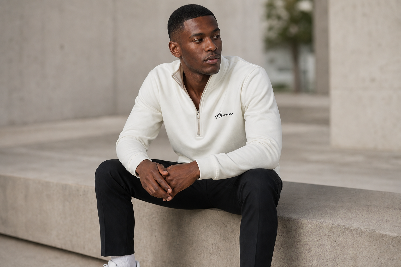 Seated model wearing the ARME cream quarter zip with black trousers