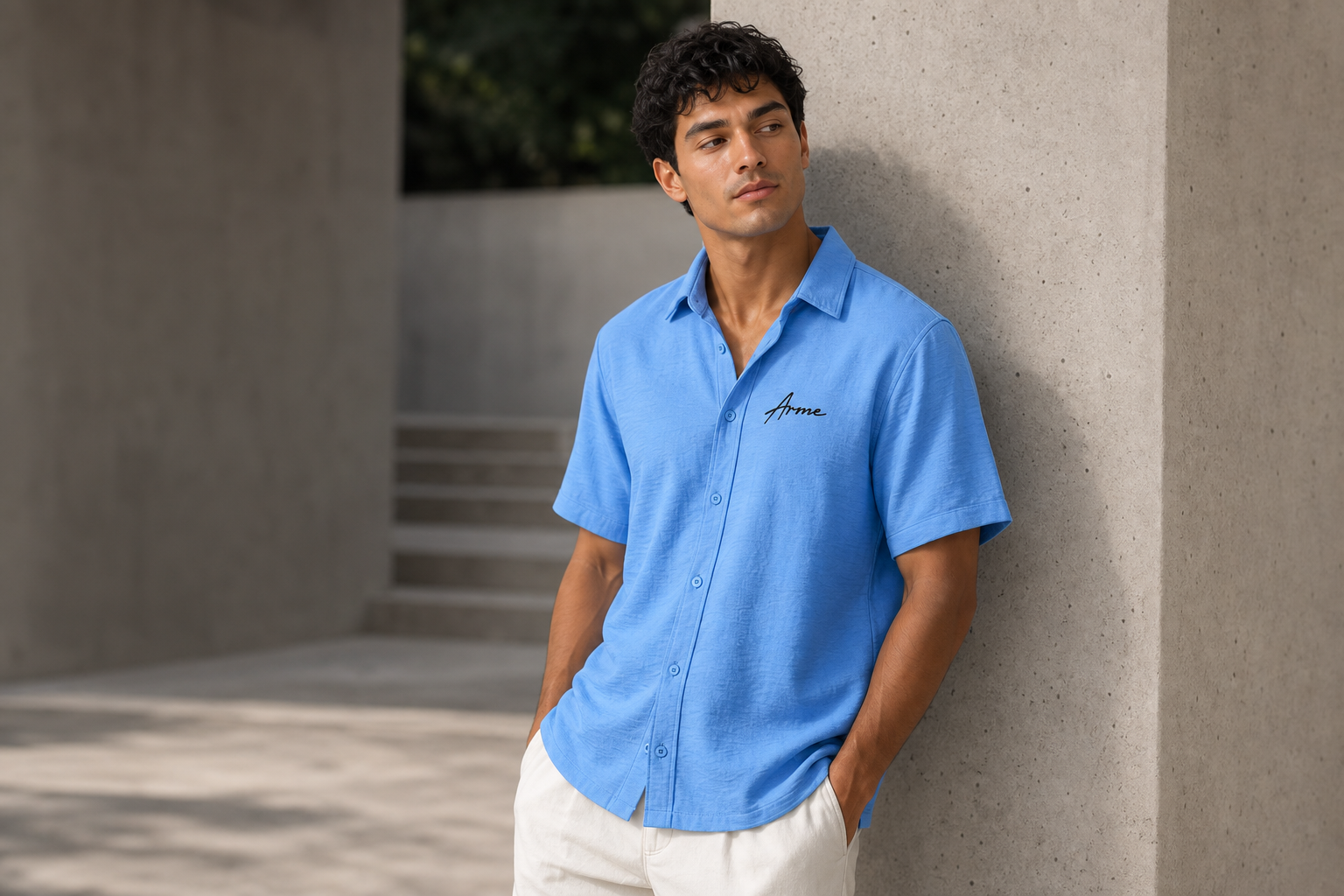 Model leaning against a concrete wall wearing the ARME baby blue Cuban button-up shirt