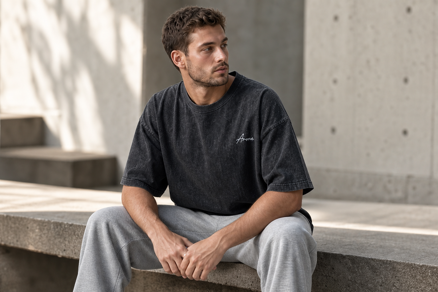 Seated model wearing the ARME oversized performance tee in washed charcoal